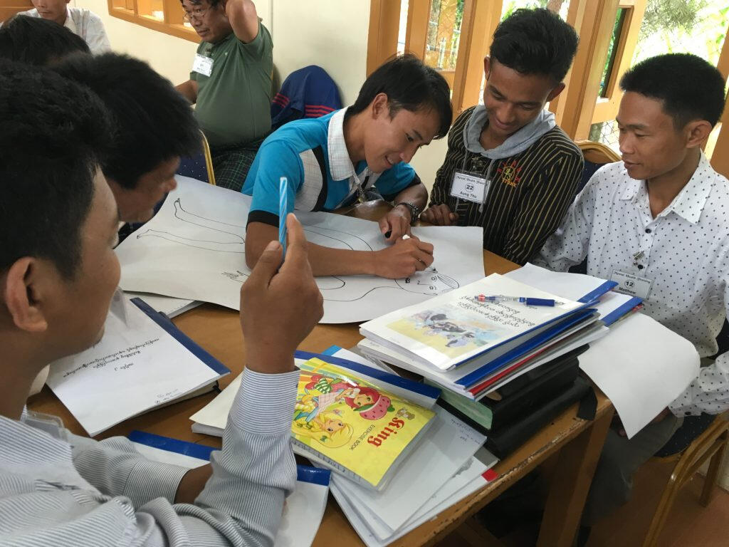 Seminar participants working as a group. One person is drawing the figure of a man as the other look on.